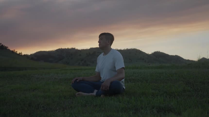 A man sits cross legged while relaxing in a large grassy field
