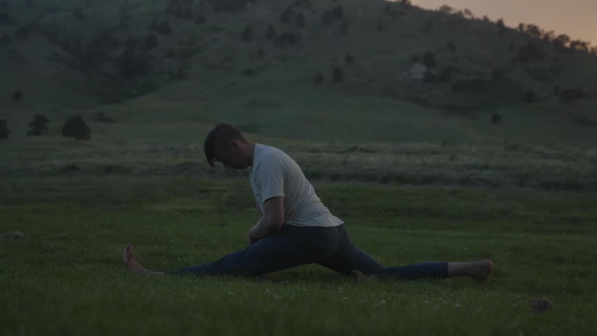 A man stretching his body on the grass in an outdoor setting with mountains