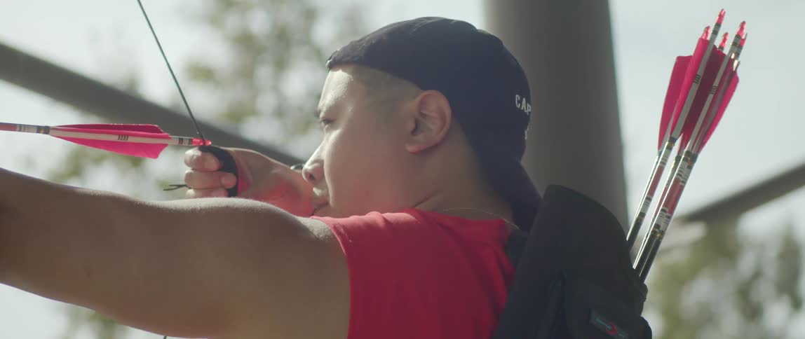 A man wearing a baseball cap strings an arrow on a sunny day