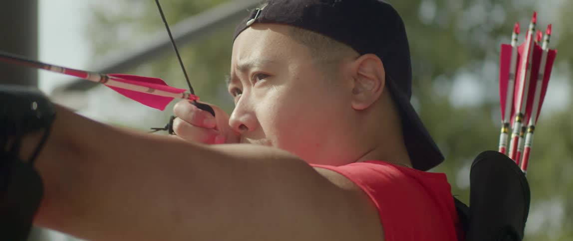 Archer standing outdoors takes aim with bow and arrow