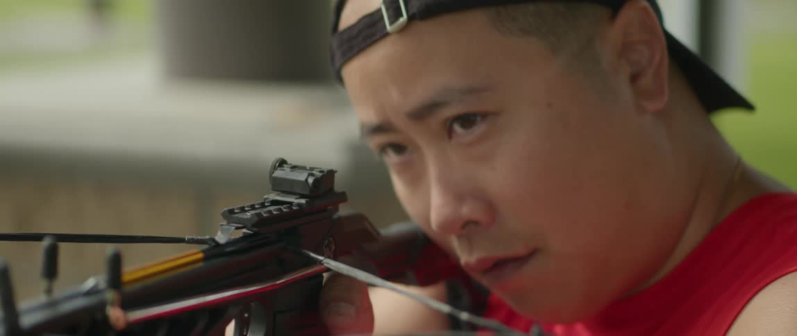 A man wearing a baseball cap holds a crossbow up and aims it