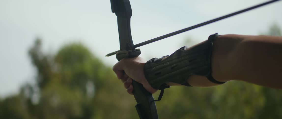 A man steadily holds a bow and shoots an arrow from it