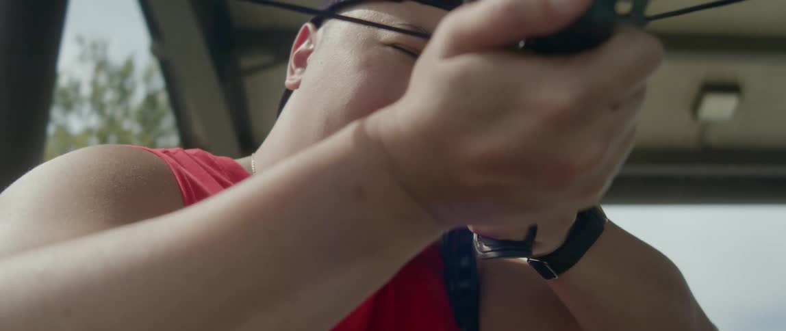 An asian man in a baseball cap is taking aim with a crossbow
