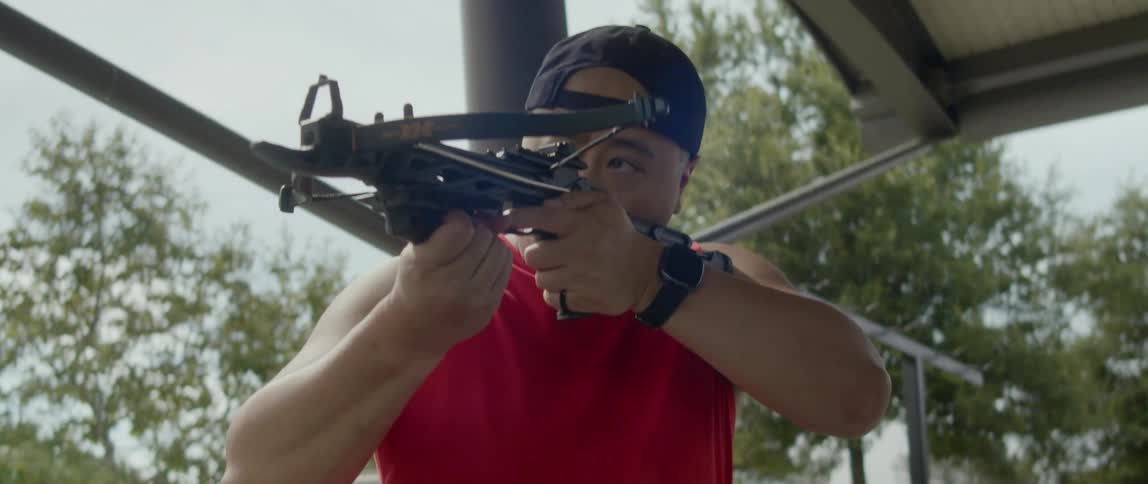 A young asian man placing an arrow on his crossbow and shooting