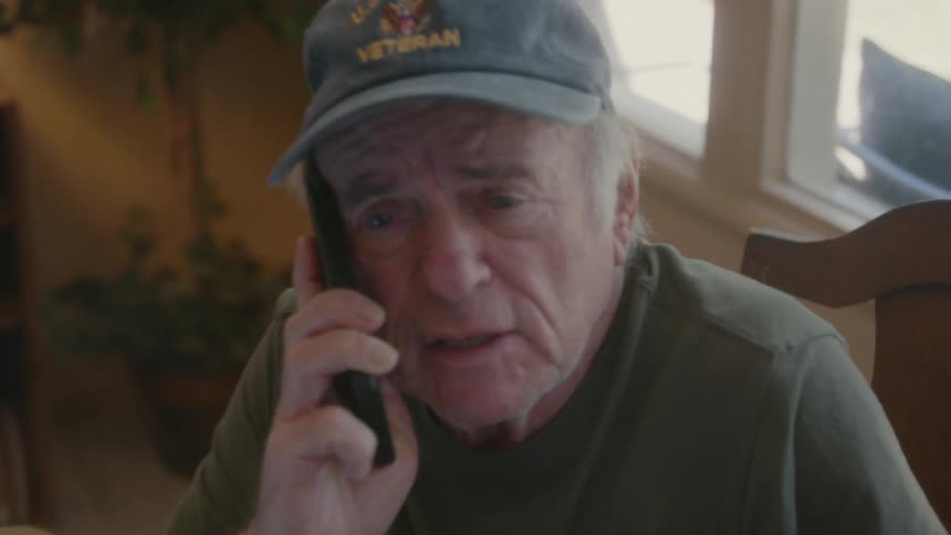 Elderly man talking on phone while sitting on a chair indoor