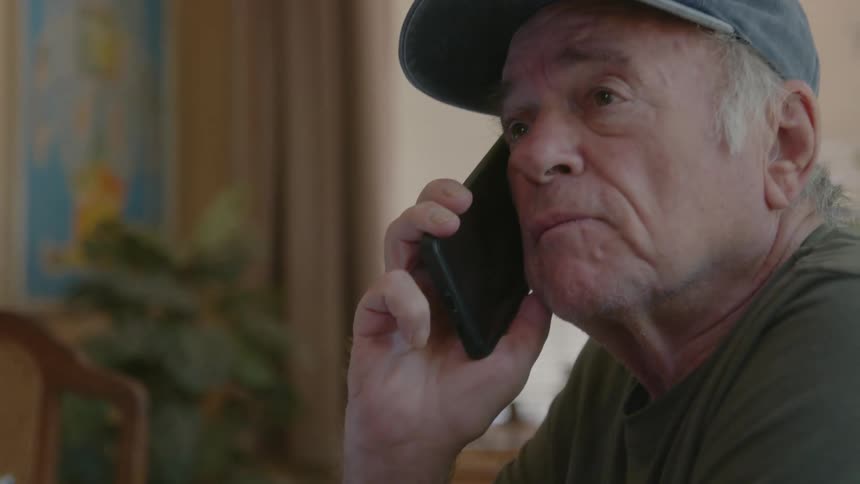 A man is talking on his cell phone with a computer on his desk