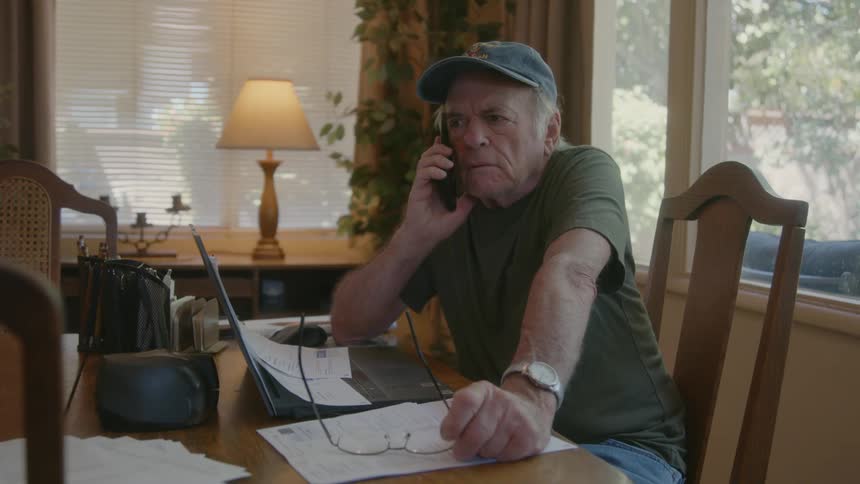Senior citizen talks on the phone while working from home