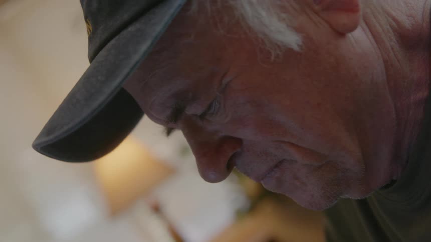 Elderly man wearing a baseball cap in the living room