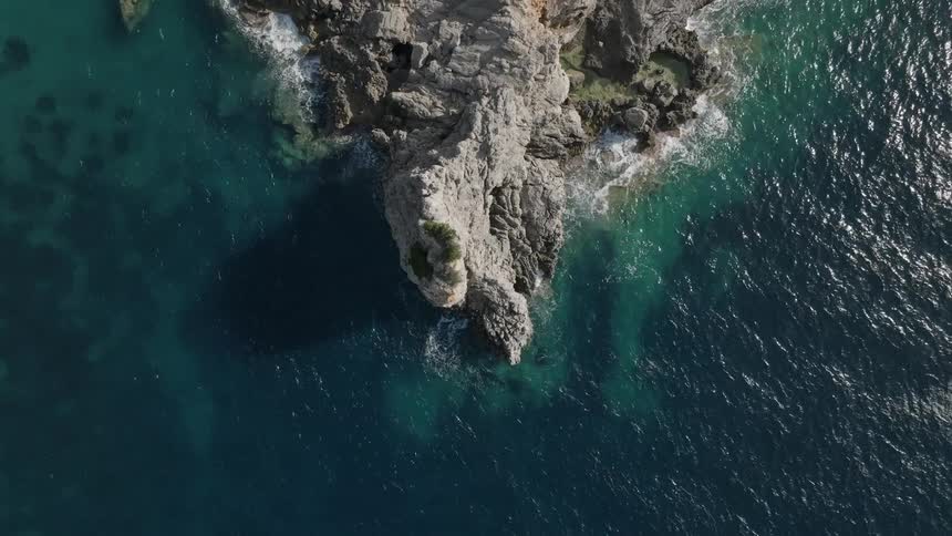 Calm ocean waters wash against a rocky promontory located at the coast