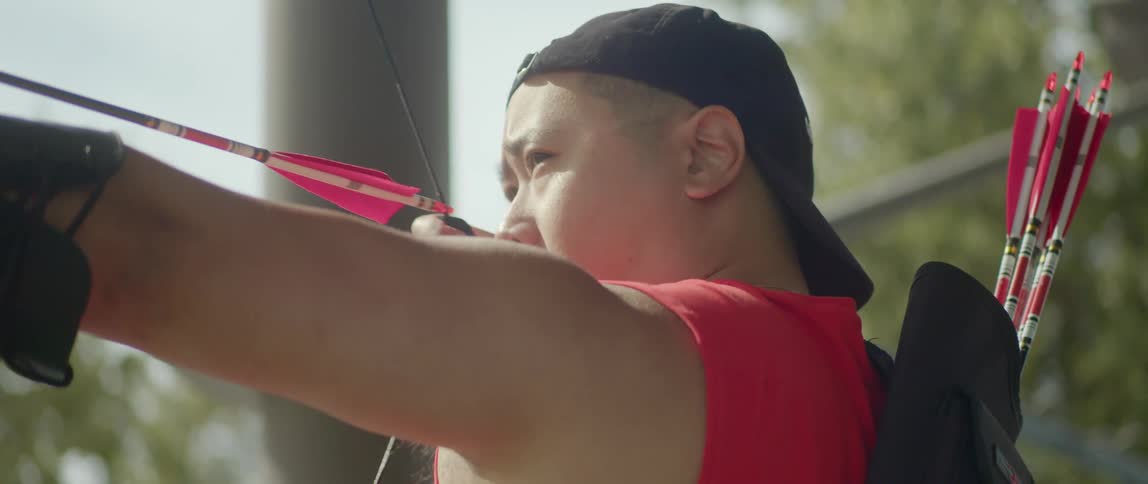 An asian man is pulling a bowstring to shoot an arrow