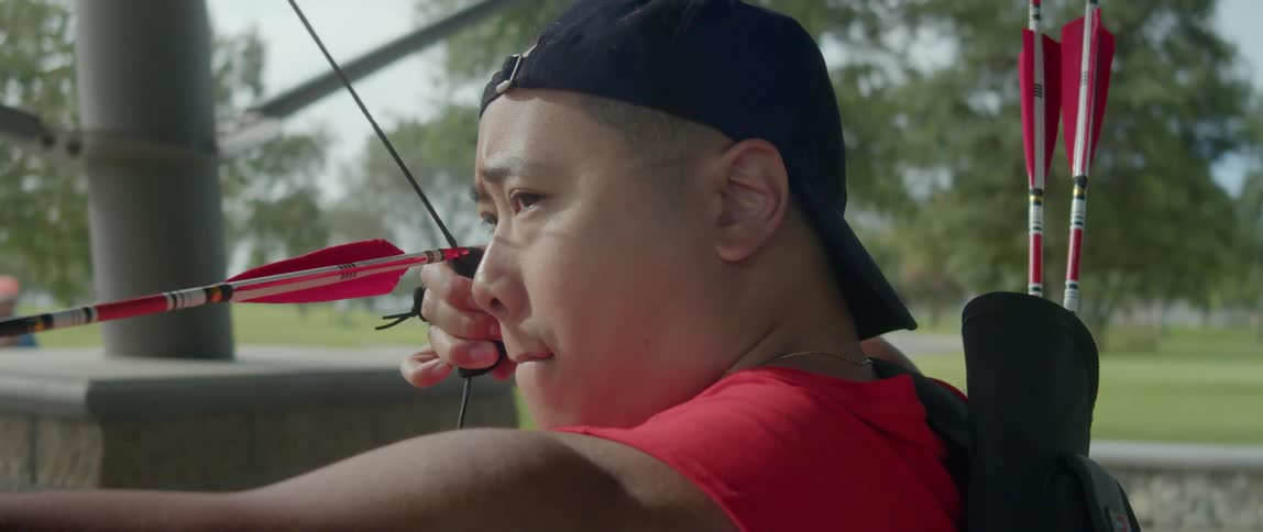 A man shoots an arrow while other men walk past behind