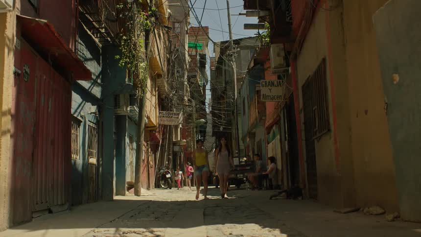 Two women walking on a street in an urban neighborhood with thirdworld housing structures
