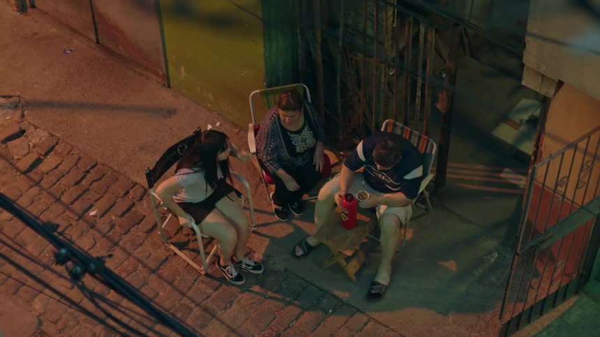 A couple sitting on chairs on the sidewalk and a girl comes and sits next to them