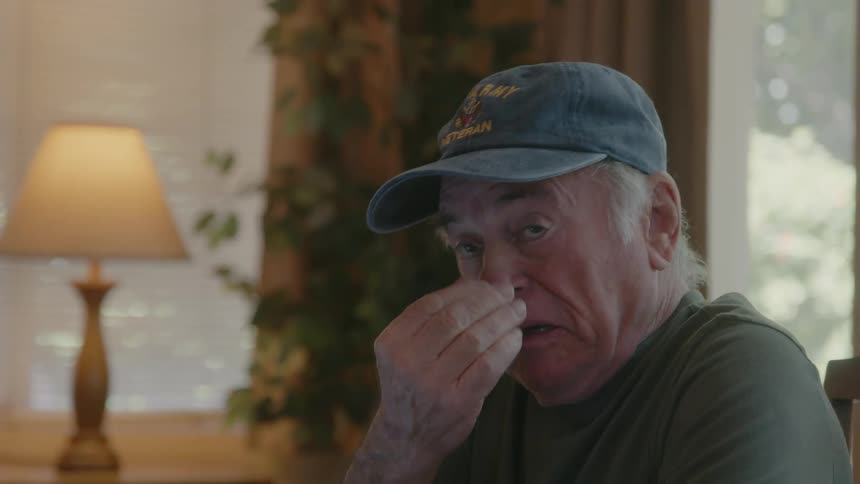 An elderly man takes off his glasses and raises his hand to his face in expressions of sadness