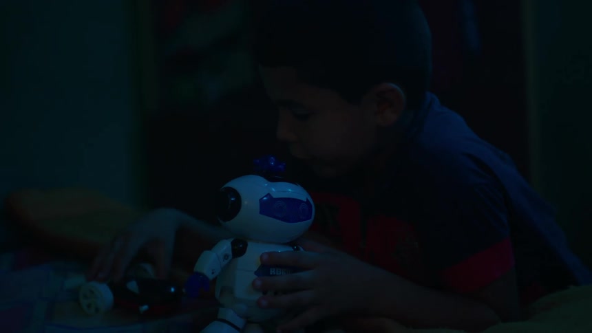A little boy playing with his toy robots in a dark room at night