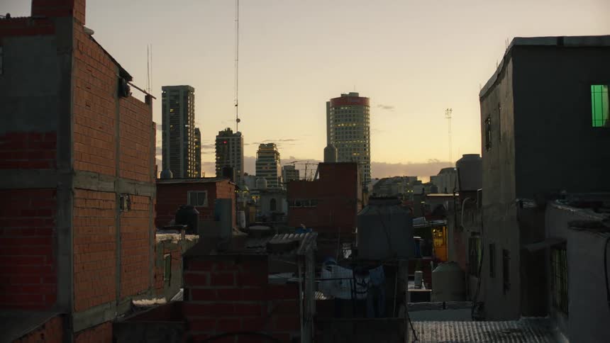 View from a rooftop of downtown towers and skyscrapers with tall antennas near the buildings as someone of the roof of a building holds up a backpack