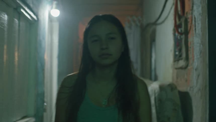 A young girl wearing a necklace is walking forward with a neutral gaze