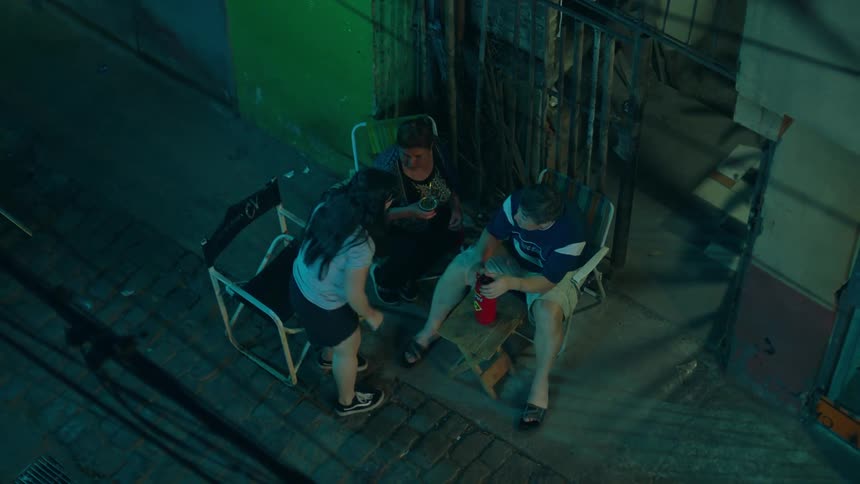 A couple is sitting on chairs in front of the house and drinking beer and then a girl arrives and sits with them