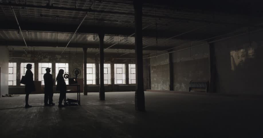 Three people watch a projection on a wall in a warehouse