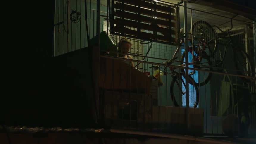 At night man talks with woman cleaning basin on balcony before walking away