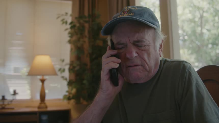 An elderly man talking on his cell phone puts on his glasses to read a paper