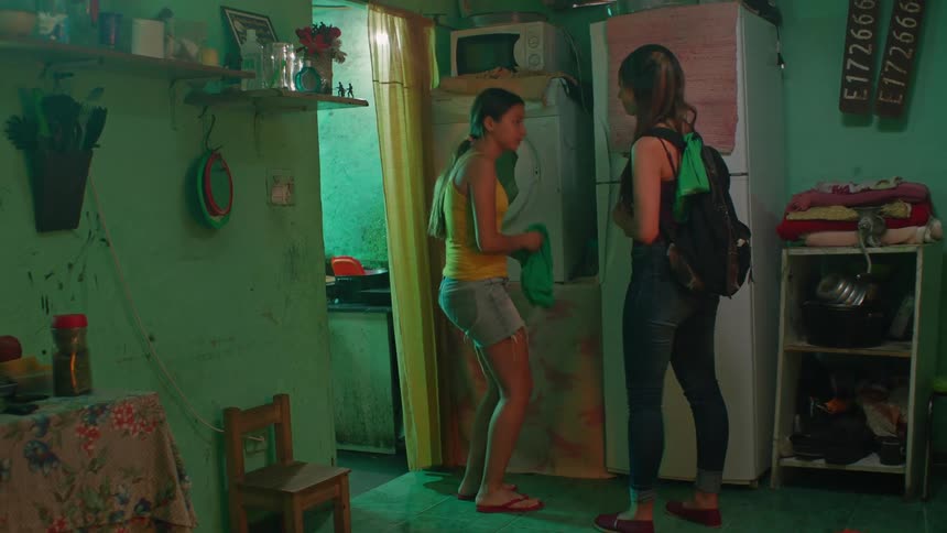After talking for some seconds one lady heads out of the room while the other lady continues doing laundry