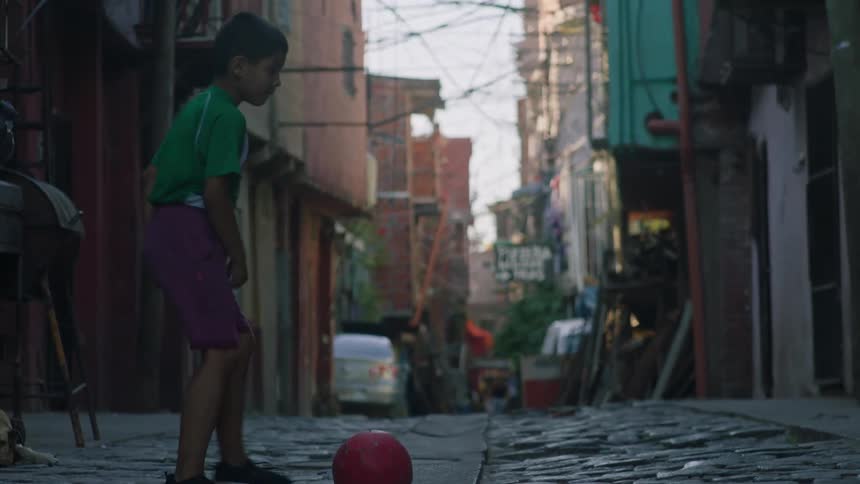 A little boy playing with a soccer ball kicking it against the wall