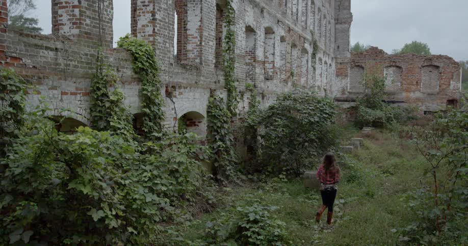 A woman is walking along a tall brick wall