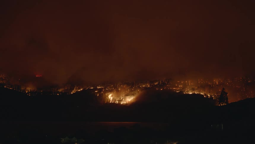 Flames rise from a blazing wildfire as the forest burns under a red smoke filled sky