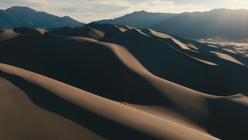 Bright sun turns mountains into silhouettes and creates dense shadows on sand dunes
