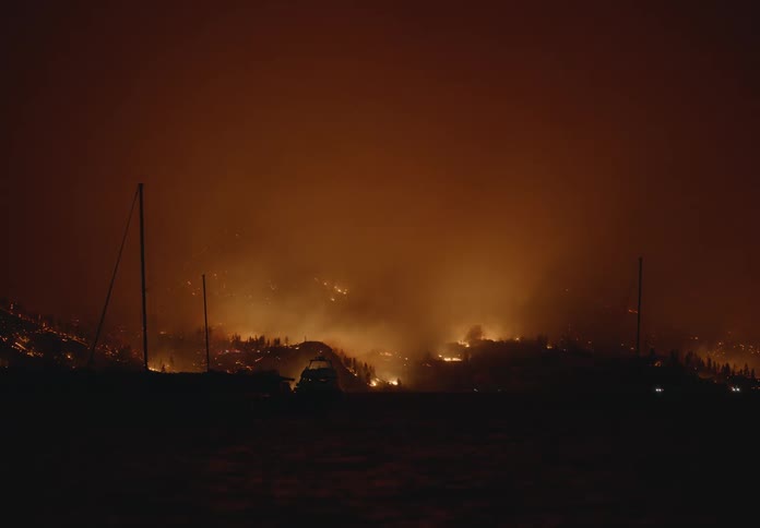 A forest fire engulfs the surrounding hills while smoke fills the night sky