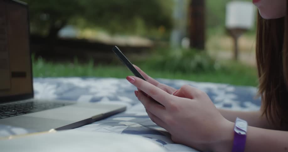 A woman is typing on a cell phone in a park during the day
