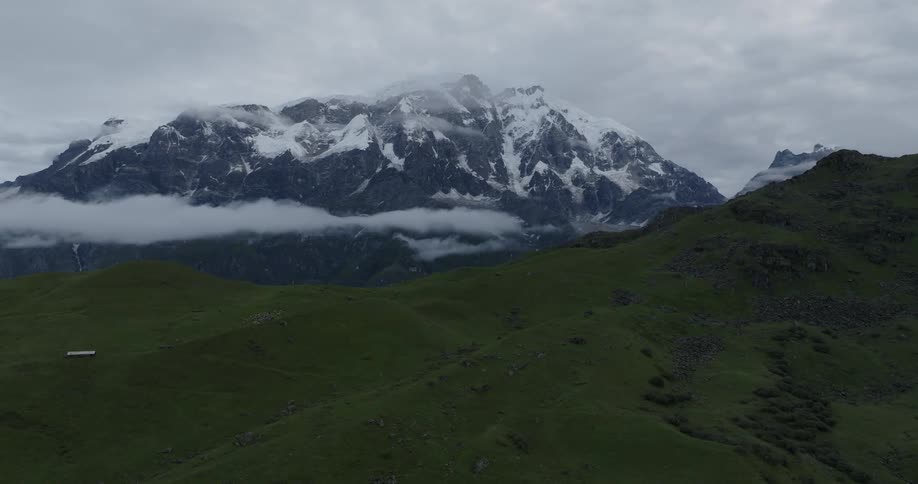 Aerial of a green mountain and a rocky mountain with snow on the peak