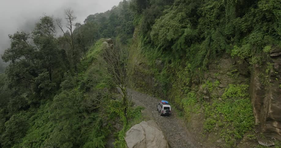 A vehicle travels along a gravel road on a mountainside on a foggy day