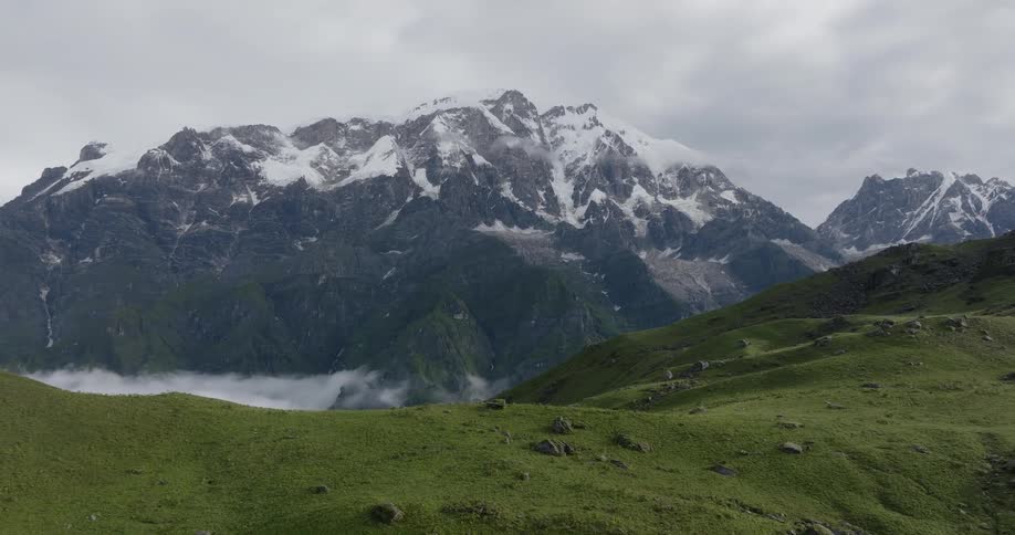 Smooth green hills lie in front of a steep mountain range on a cloudy day