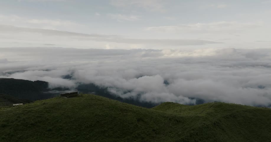 Aerial of grass covered mountain peaks with rural structures on the hillside with dense clouds in the sky