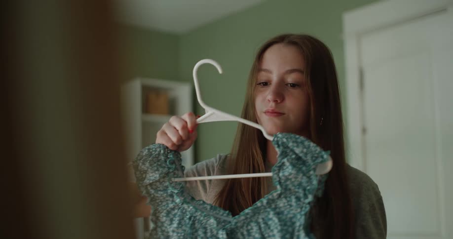 Teenage girl holding two different dresses up to the mirror indoor