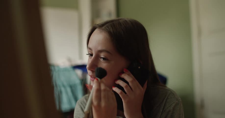 A teenage girl puts on makeup while using the phone