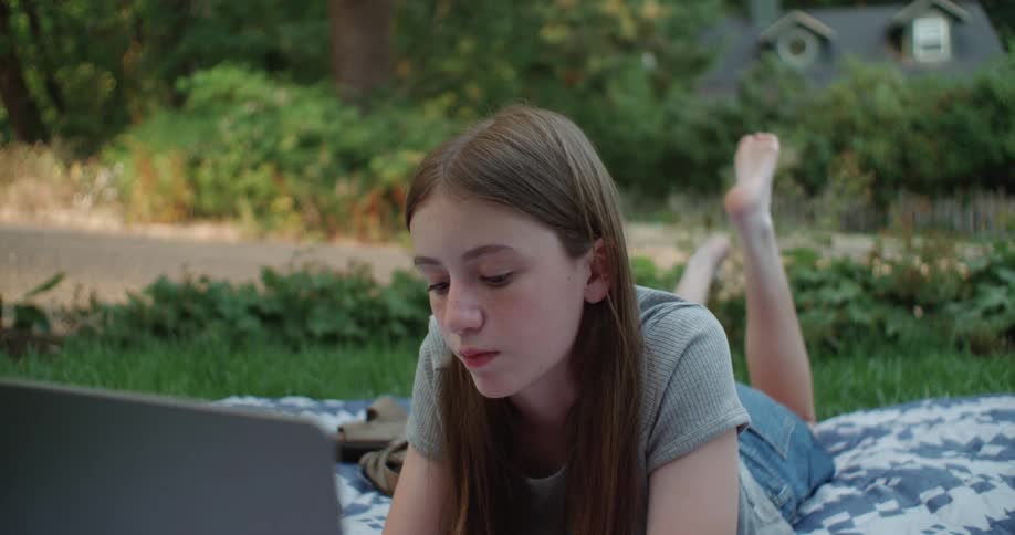 A girl lying in the garden working on her laptop