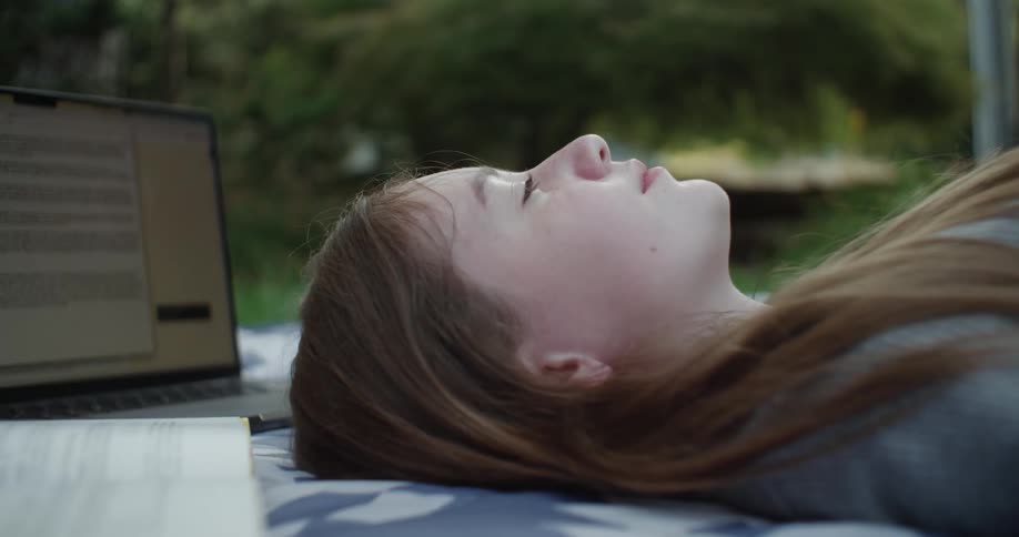 Teenage girl laying down on a blanket near her laptop on a bright day
