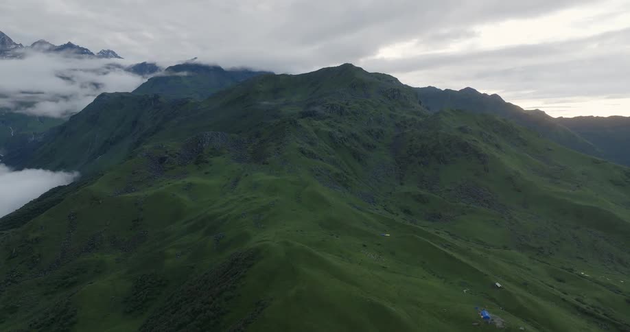 Drone view of grass covered mountain ranges with peaks covered in fog