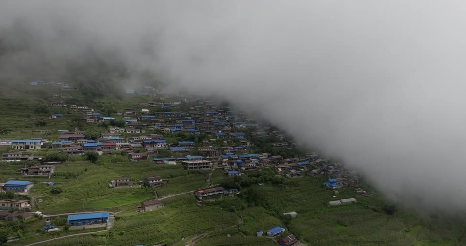 Houses and apartment buildings of a mountainside community are seen through the clouds