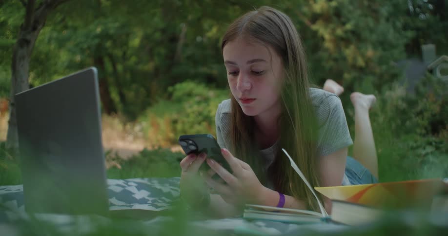 A teenage girl is lying on the lawn and texting in her cell phone