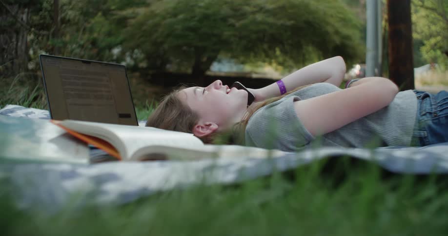 Young girl lying on a blanket on the grass and talking on her cellphone