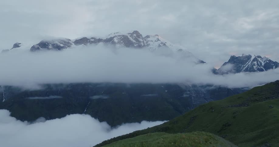 Drone view of grass and snow covered mountain peaks with fog settling in the valley between them