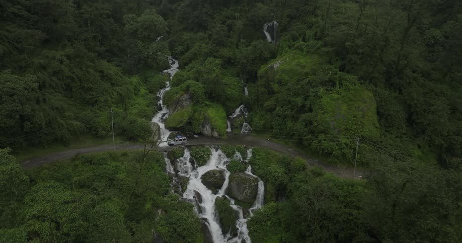 A car driving along a dirt road that passes a small waterfall