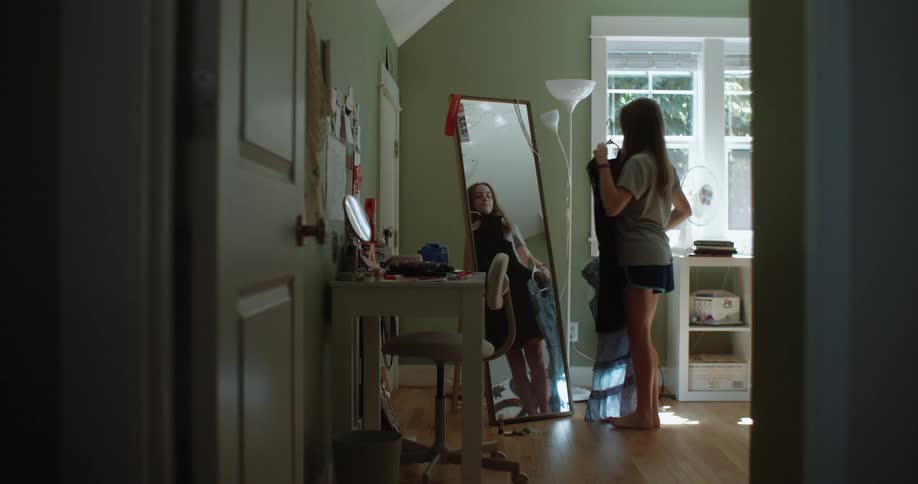 Teenage girl tries dresses in front of a mirror in her bedroom