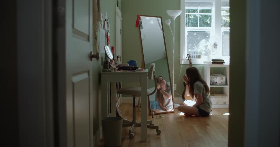 Teenage girl sits crosslegged in front of mirror and puts on makeup