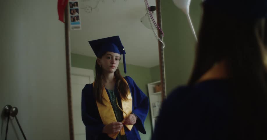 A teenage girl in prom clothes is looking at herself in a mirror
