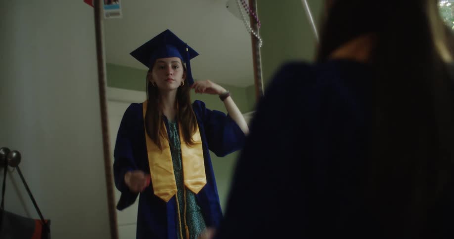 Teenage girl tries on graduate gown and checks her appearance in mirror